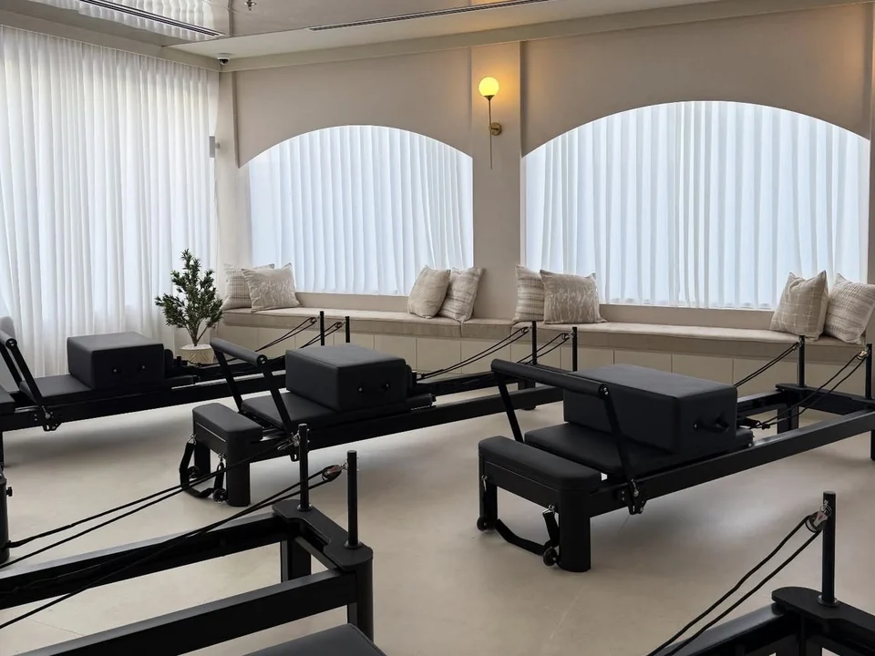 Black Pilates reformers arranged beside sheer curtains and cushioned window seating at Elevate.